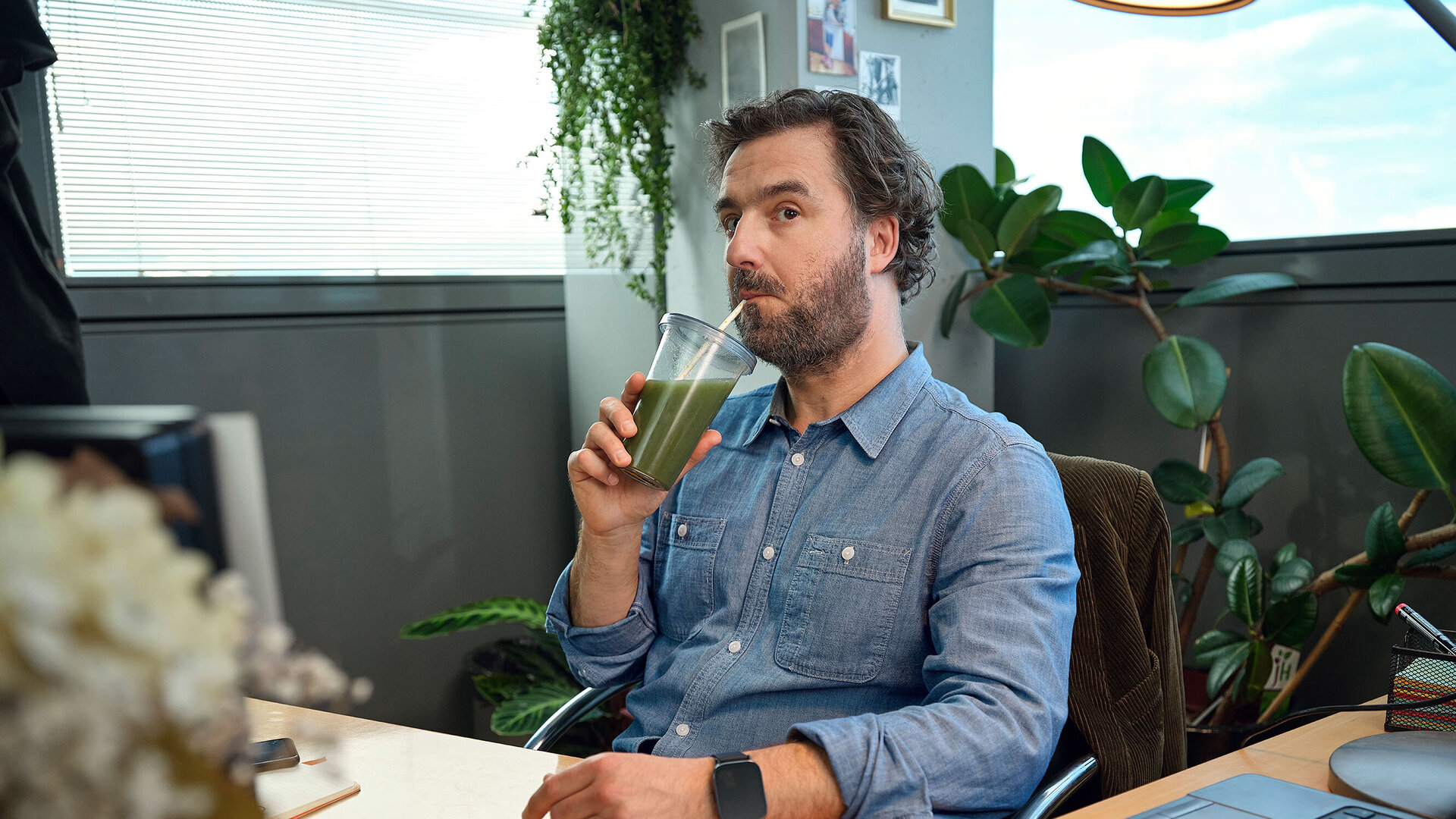 Mann sitzt im Büro und trink einen grünen Saft.