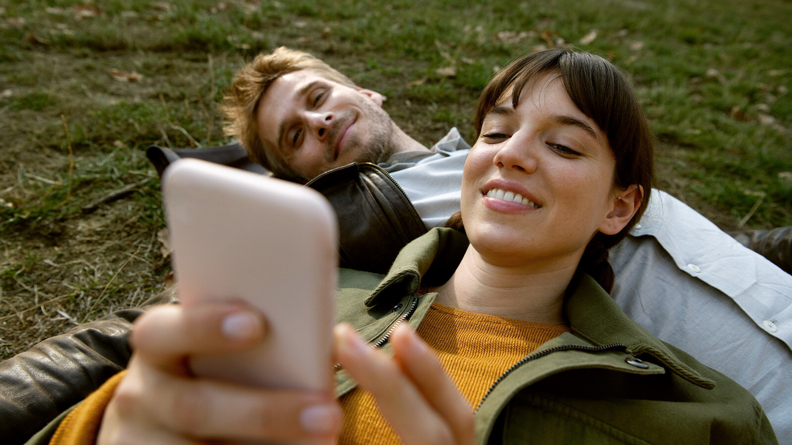 Frau und Mann liegen auf einer Wiese. Die Frau schaut auf ihr Smartphone
