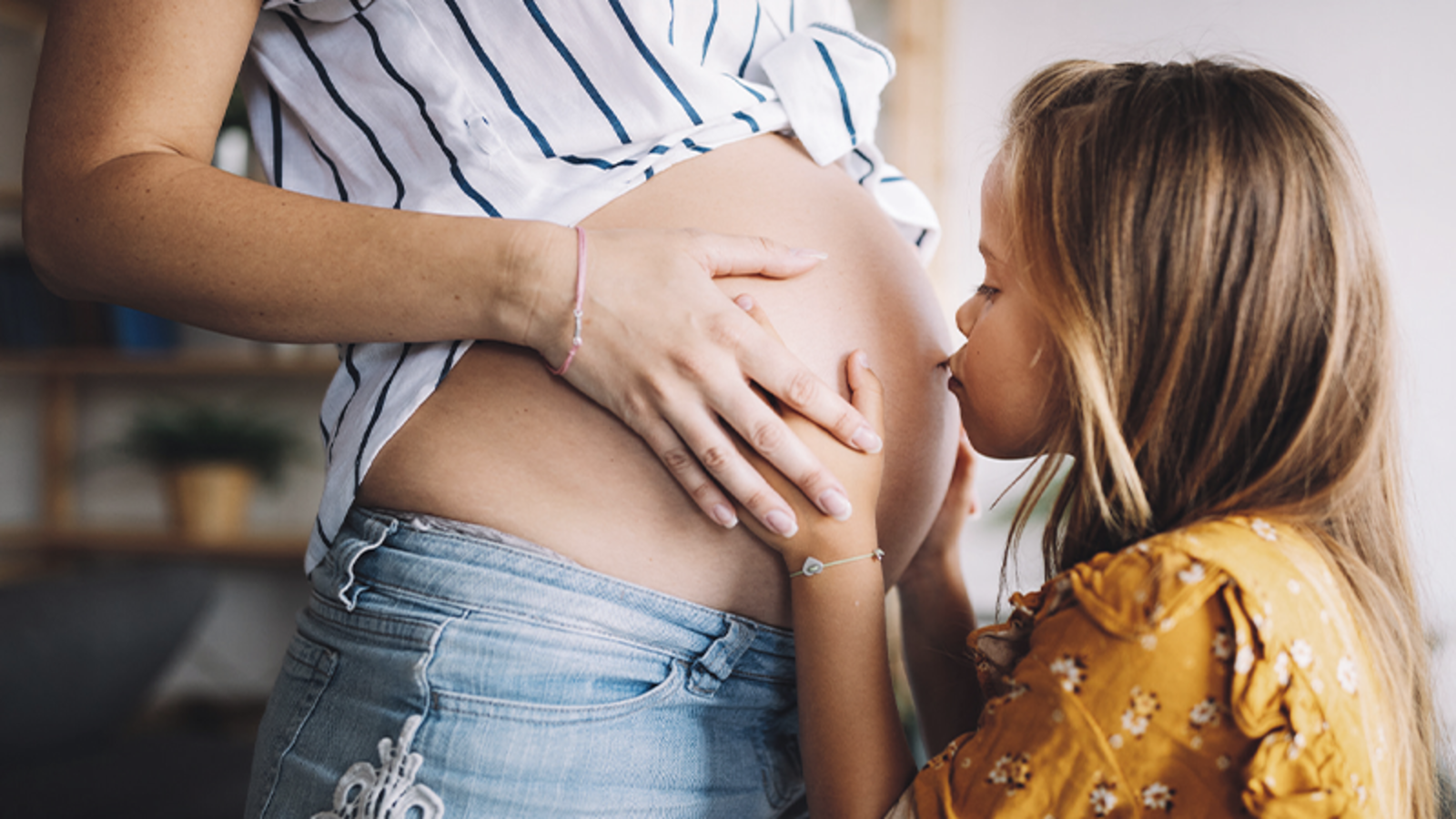 Kleines Mädchen küsst den Schwangerschaftsbauch ihrer Mama