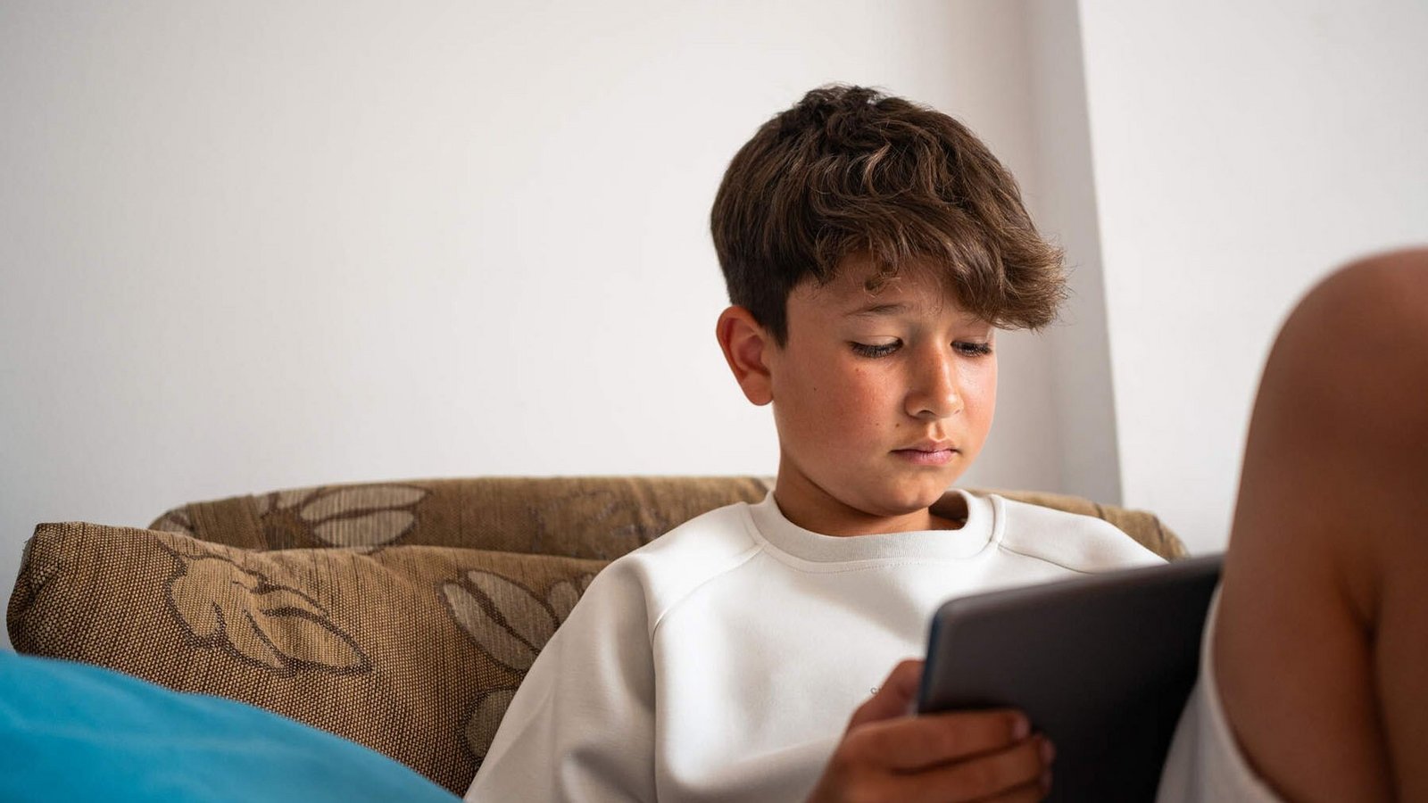 Junge sitzt auf dem Sofa und schaut in sein Tablet.