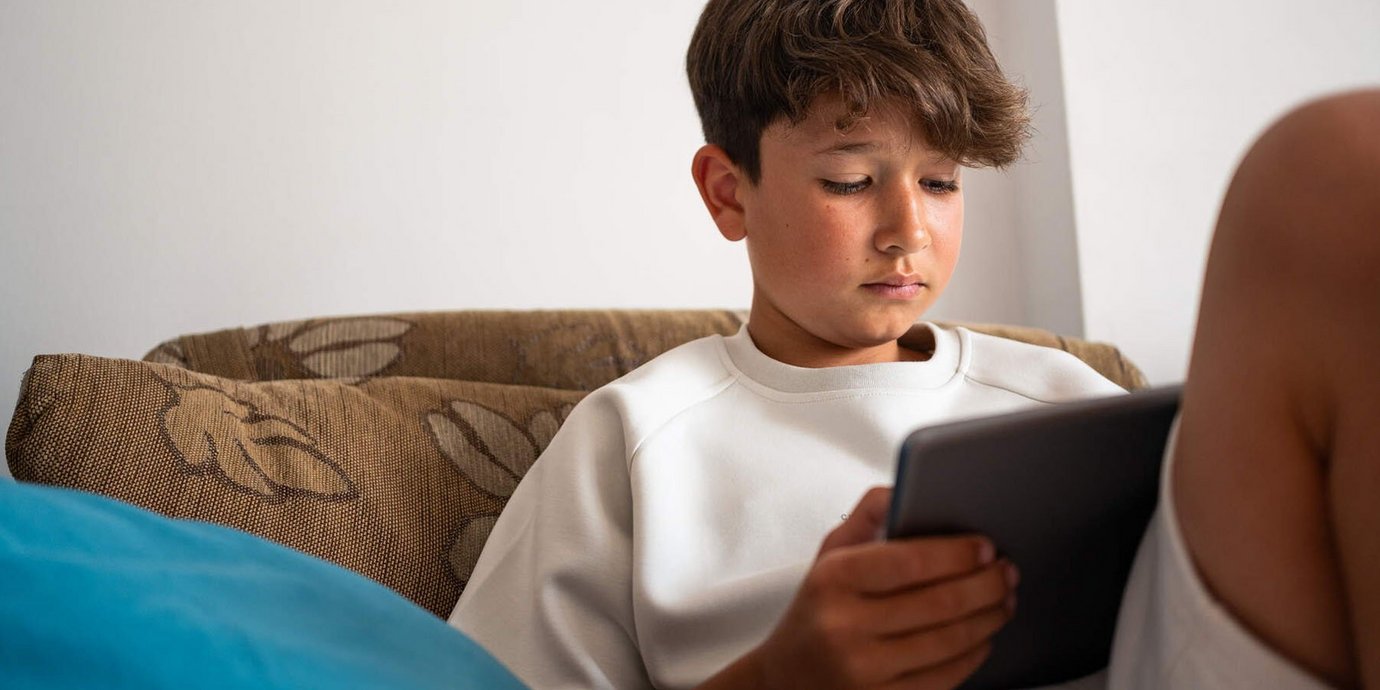 Junge sitzt auf dem Sofa und schaut in sein Tablet.