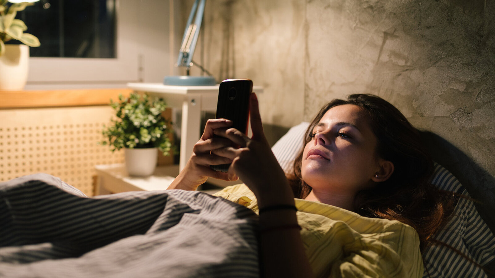 Frau scroll durch ihr Handy liegend im Bett