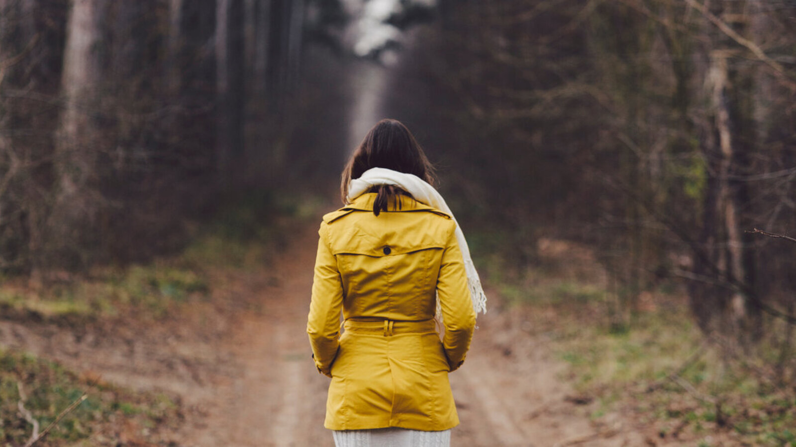 Frau in gelber Regenjacke geht durch einen Wald spazieren.