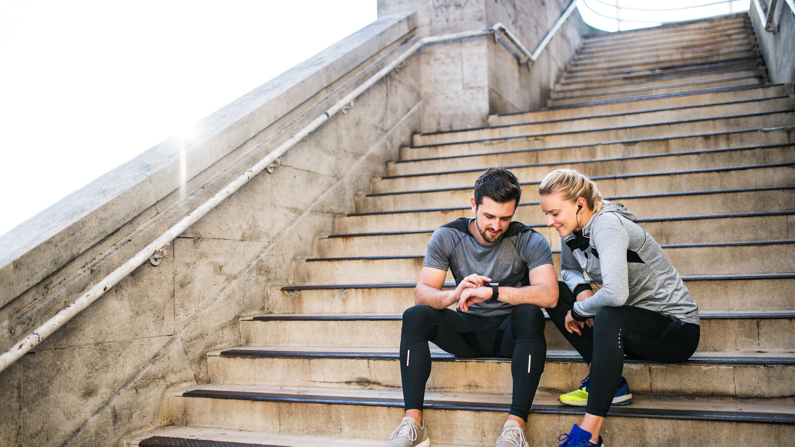 Mann sitzt mit Frau auf einer Treppe. Beide gucken gemeinsam auf die Smartwatch des Mannes.