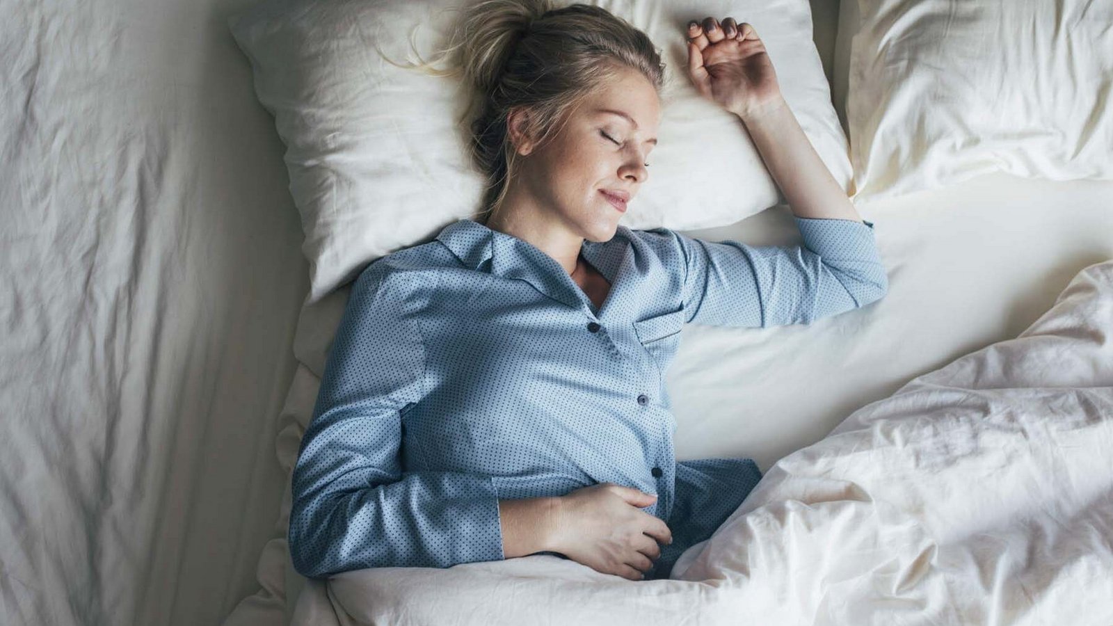 Frau im blauen Pyjama schläft zufrieden im Bett.