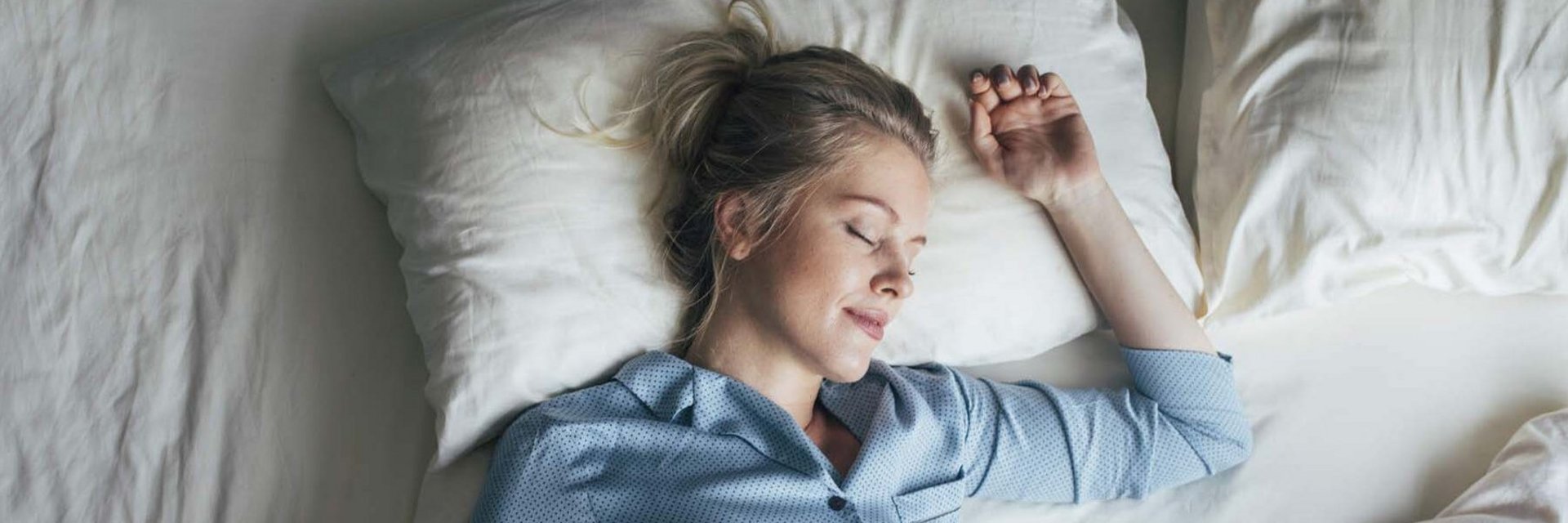 Frau im blauen Pyjama schläft zufrieden im Bett.