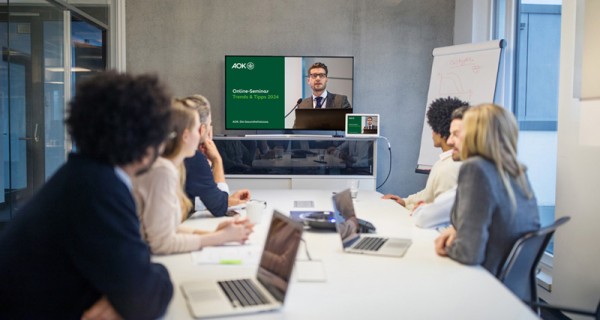 Konferenzraum und sechs Personen schauen auf ein Online-Seminar