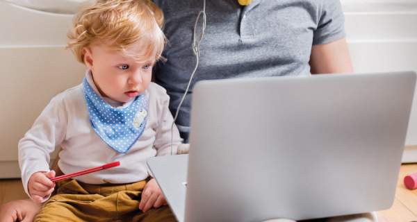 Ein kleiner Junge hat einen Stift in der Hand und schaut mit seinem Papa auf einen Laptop.