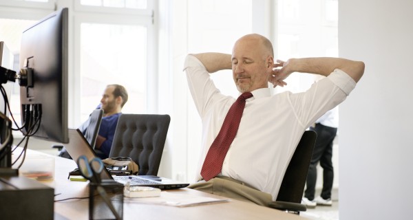 Geschäftsmann im Anzug lehnt sich am Arbeitsplatz entspannt zurück