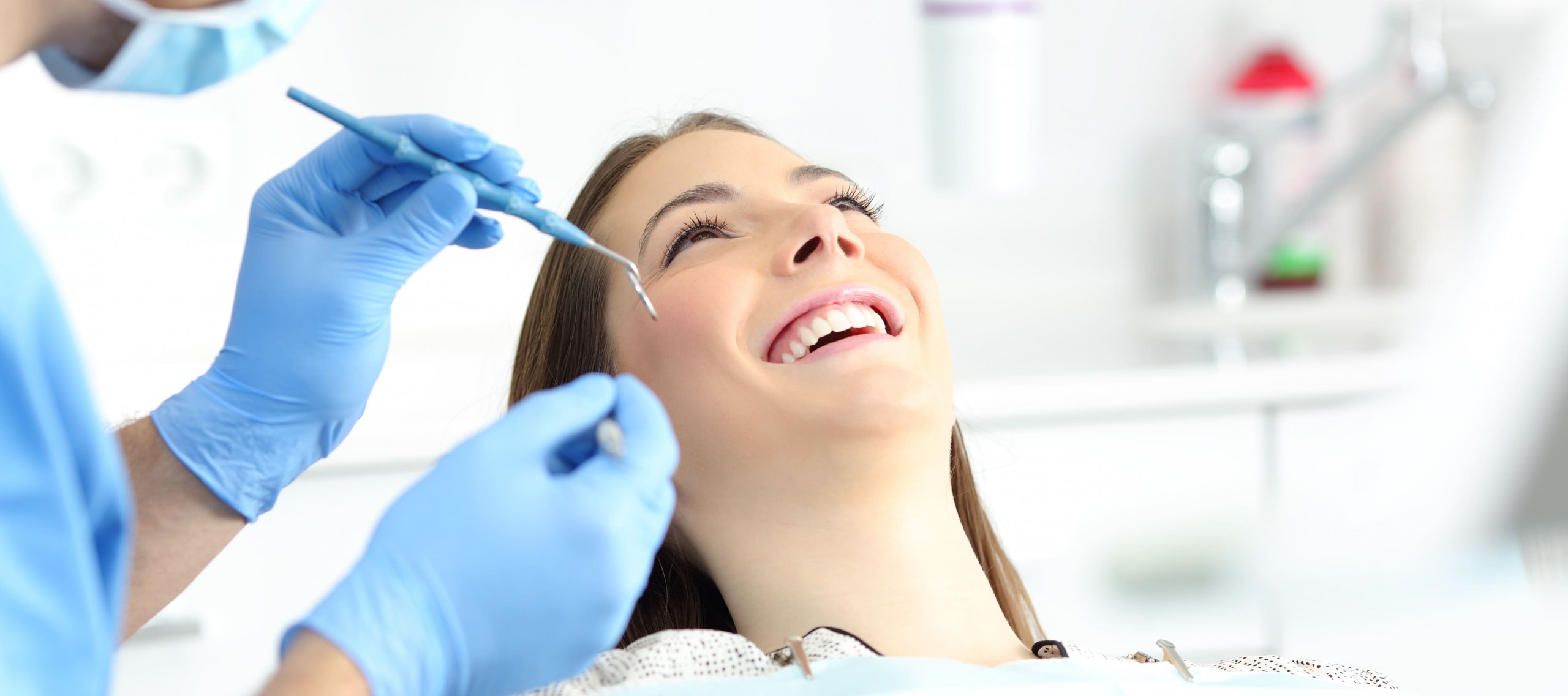 Frau sitzt lächelnd auf dem Zahnarztstuhl und wartet, dass der Zahnarzt mit der Zahnreinigung beginnt.