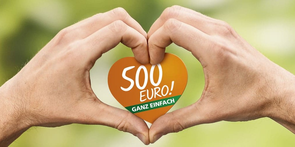 Zwei Hände formen ein Herz um ein herzförmiges Papier mit dem 500 Euro Logo darauf.