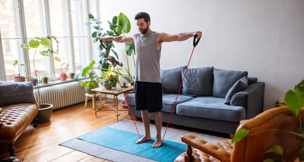 Mann und Frau machen zu Hause Yoga-Übungen und schauen dabei auf ein Laptop.