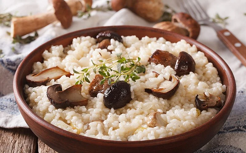 Braune Schale mit cremigem Risotto und Pilzstücken garniert mit frischem Thymian.