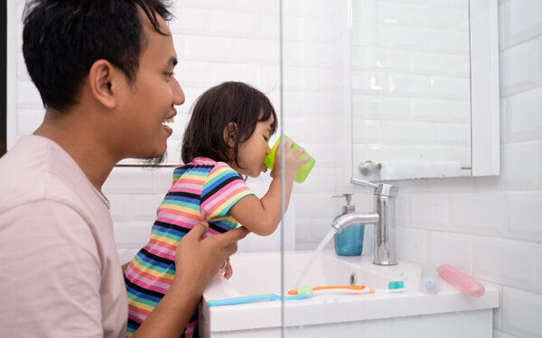 Ein Vater hilft seiner kleinen Tochter nach dem Zähneputzen, den Mund gründlich auszuspülen.