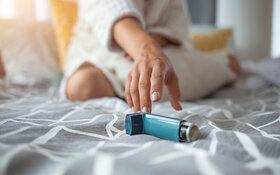Eine Frau sitzt auf dem Bett und greift zu ihrem Asthmaspray.