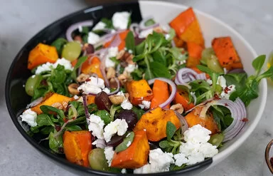 Kürbissalat mit Feta nach einem Rezept von Felicitas Then, angerichtet auf einem schwarz-weißen Teller, garniert mit Weintrauben und Zwiebeln.