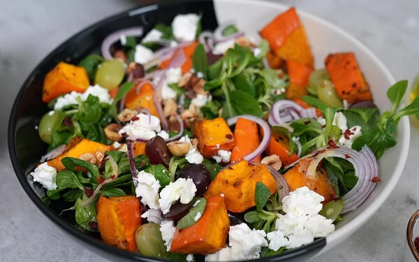 Kürbissalat mit Feta nach einem Rezept von Felicitas Then, angerichtet auf einem schwarz-weißen Teller, garniert mit Weintrauben und Zwiebeln.