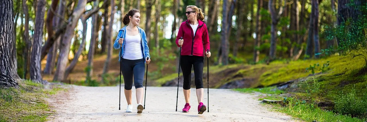 Zwei Frauen beim Nordic Walking im Wald mit Trekkingstöcken.