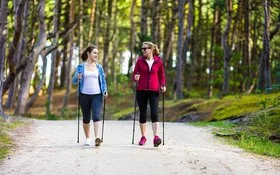 Zwei Frauen beim Nordic Walking im Wald mit Trekkingstöcken.