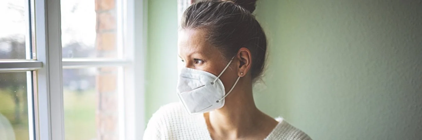 Eine Frau ist zu Hause und trägt eine FFP2-Maske. Erfahren Sie mehr über die Quarantäneregeln während der Corona-Pandemie.