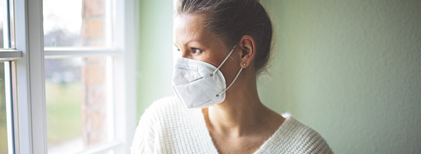 Eine Frau ist zu Hause und trägt eine FFP2-Maske. Erfahren Sie mehr über die Quarantäneregeln während der Corona-Pandemie.