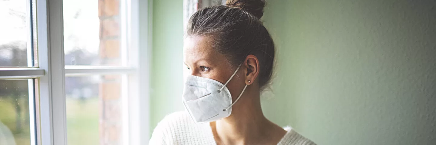 Eine Frau ist zu Hause und trägt eine FFP2-Maske. Erfahren Sie mehr über die Quarantäneregeln während der Corona-Pandemie.