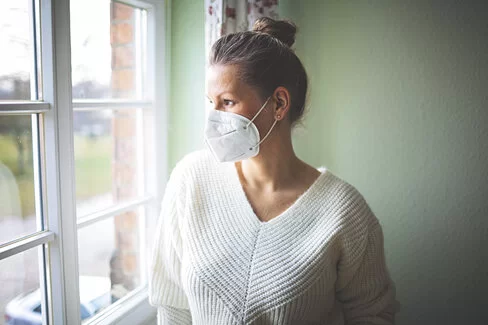 Eine Frau ist zu Hause und trägt eine FFP2-Maske. Erfahren Sie mehr über die Quarantäneregeln während der Corona-Pandemie.