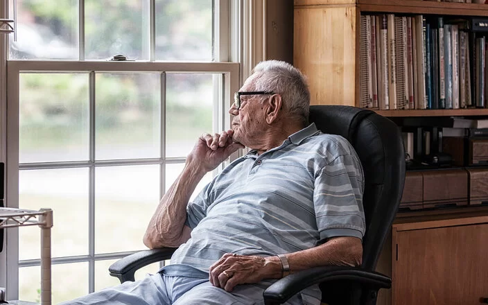 Ein älterer Mann sitzt in einem Lehnstuhl und schaut aus dem Fenster.