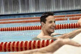 Zwei Männer halten sich am Beckenrand eines Schwimmbeckens fest und lachen. Sie nehmen an einem AOK Gesundheitskurs teil.