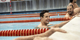 Zwei Männer halten sich am Beckenrand eines Schwimmbeckens fest und lachen. Sie nehmen an einem AOK Gesundheitskurs teil.