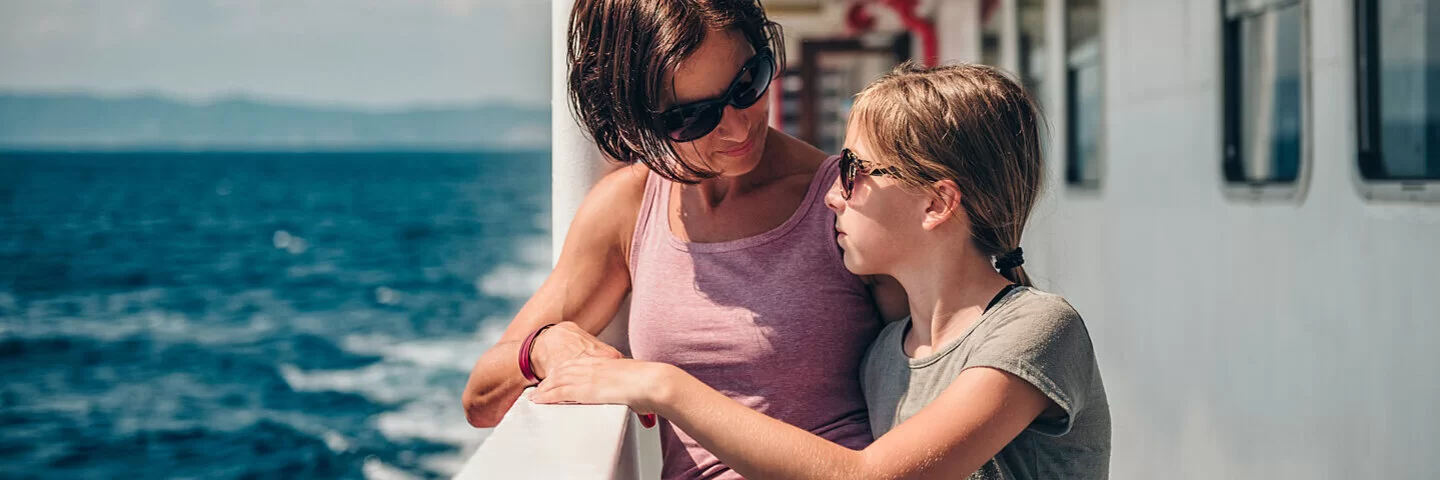 Mutter steht mit ihrer seekranken Tochter an der Schiffsreling.