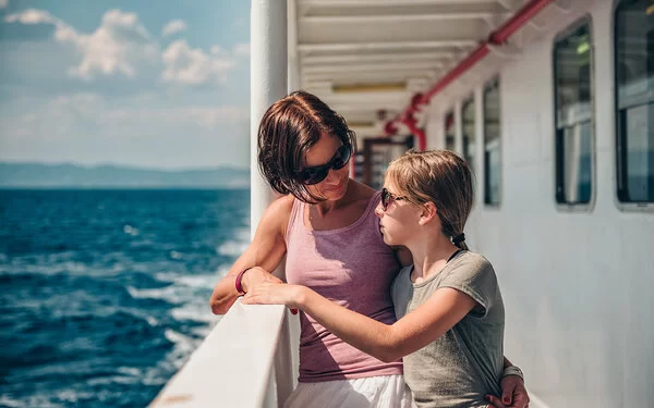 Mutter steht mit ihrer seekranken Tochter an der Schiffsreling.