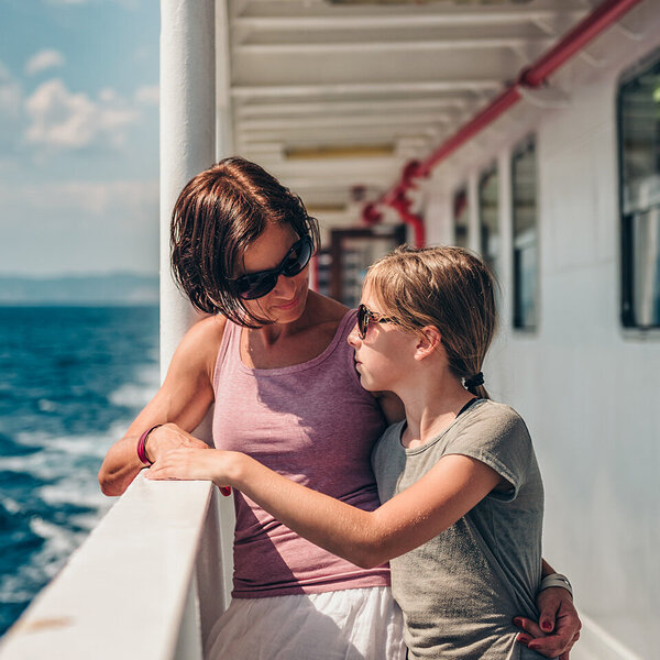 Mutter steht mit ihrer seekranken Tochter an der Schiffsreling.