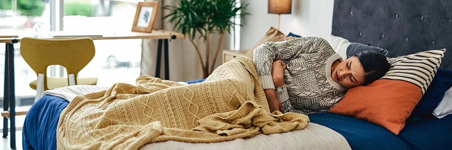 Eine Frau liegt mit Salmonellenvergiftung im Bett und hält sich den Bauch.