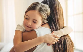 Mutter trägt Tochter mit Wachstumsschmerzen auf dem Arm, die Tochter umarmt die Mutter mit geschlossenen Augen und lächelt.