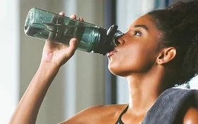 Eine Frau trinkt Wasser aus einer Flasche aus, denn sie weiß, dass man viel trinken muss.