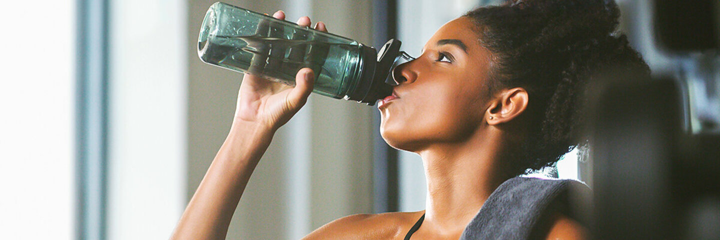 Eine Frau trinkt Wasser aus einer Flasche aus, denn sie weiß, dass man viel trinken muss.
