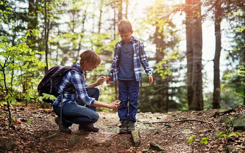 Eine Mutter sprüht ihren Sohn mit Anti-Zecken-Spray bei einem Spaziergang durch den Wald ein.