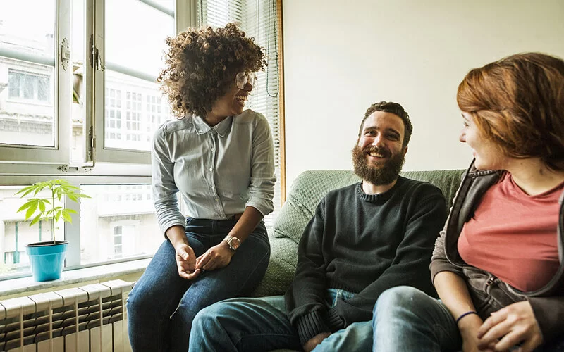 Zwei Frauen und ein Mann sitzen gemeinsam auf einem Sofa am Fenster und sprechen über Co-Parenting.