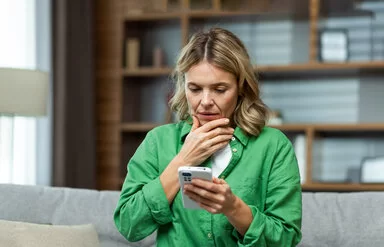 Eine Frau blickt nachdenklich auf ihr Smartphone, das sie in der Hand hält.