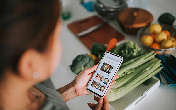 Frau blickt auf Smartphone und nutzt die individuelle Ernährungsberatung der Oviva-App.