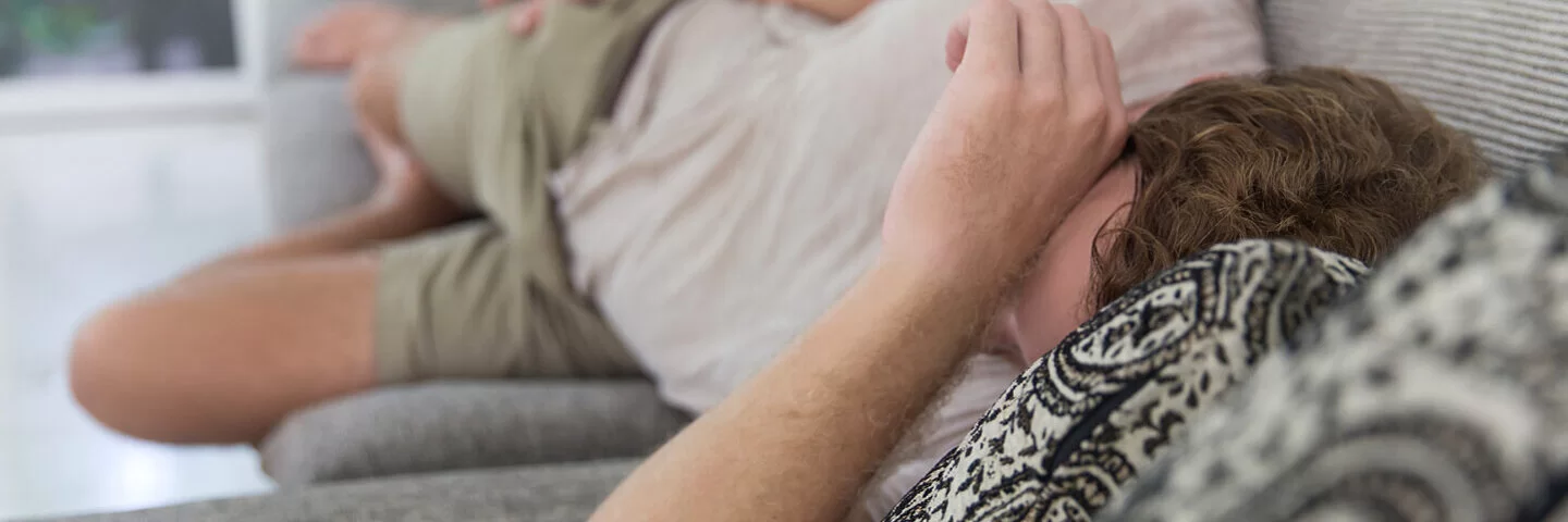 Ein Mann liegt erschöpft und mit Schmerzen auf der Couch.