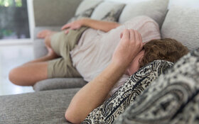 Ein Mann liegt erschöpft und mit Schmerzen auf der Couch.