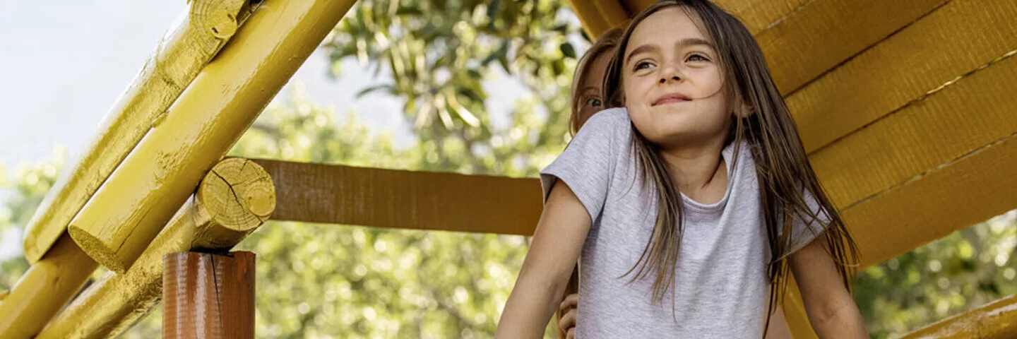 Ein junges Mädchen steht in einem Baumhaus und lächelt. Hinter ihr steht eine Frau. Kuren für Kinder können chronischen Krankheiten vorbeugen.