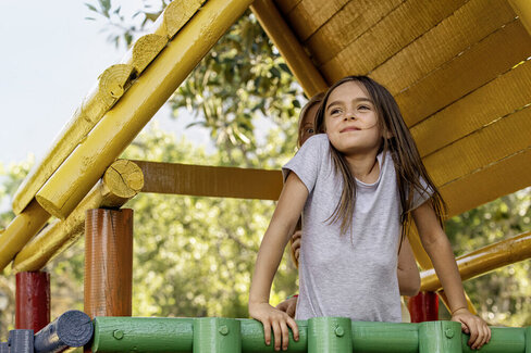 Ein junges Mädchen steht in einem Baumhaus und lächelt. Hinter ihr steht eine Frau. Kuren für Kinder können chronischen Krankheiten vorbeugen.