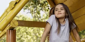 Ein junges Mädchen steht in einem Baumhaus und lächelt. Hinter ihr steht eine Frau. Kuren für Kinder können chronischen Krankheiten vorbeugen.