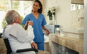 Eine Pflegeperson unterstützt einen älteren Mann im Rollstuhl beim Zähneputzen.