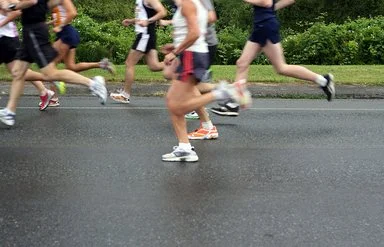 Läufergruppe in Sportkleidung läuft auf nasser Straße bei einem Firmenlauf