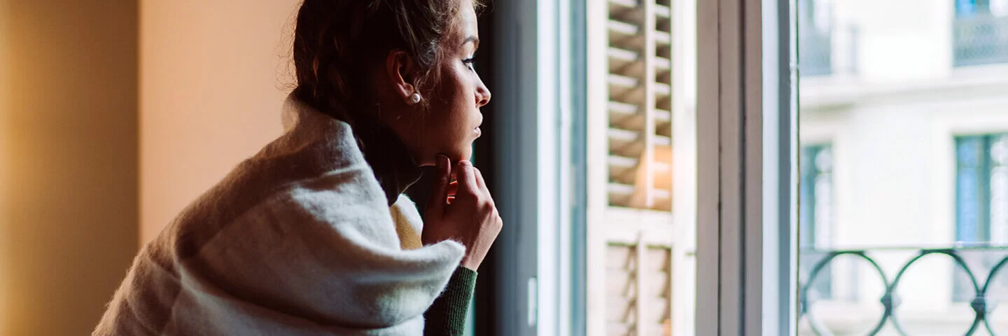 Eine junge Frau mit psychischen Problemen schaut betrübt aus dem Fenster.