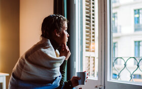 Eine junge Frau mit psychischen Problemen schaut betrübt aus dem Fenster.